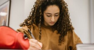 Young woman writing in classroom with smartphone in hand, studying.