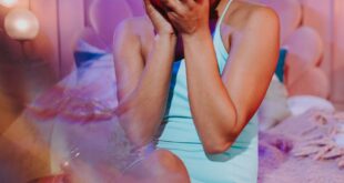 Smiling woman holding a camera in a cozy, softly lit room with neon text.