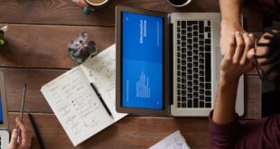 Group of coworkers discussing business strategies with laptops and tablets in a modern office setting.