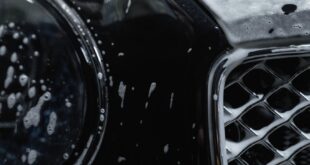 Detailed view of a luxury black car covered with soap suds during a wash.