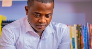 African man focused on using his smartphone while seated in a modern office with a bookshelf backdrop.