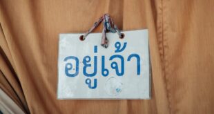 A Thai language sign hangs on brown fabric, conveying a message in Chiang Mai, Thailand.