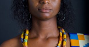 Elegant portrait of a woman in vibrant traditional Ghanaian clothing against a dark studio background.