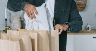 Adult man organizing purchases with paper bags and laptop in a modern home setting.