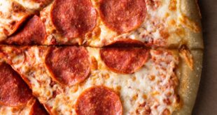 Close-up of a hot pepperoni pizza sliced vertically on a cardboard background.
