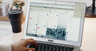 Hands typing on a laptop in a modern office setting with notes and task management software visible on the screen.