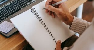 Man writing in notebook with laptop and coffee in home office setting.