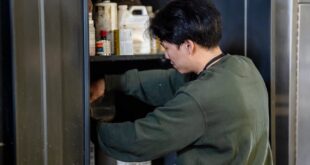 A man organizes chemicals and supplies in an industrial storage cabinet.