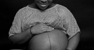A joyful pregnant woman smiles warmly, embracing her belly in a studio setting.