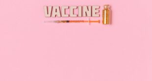 Conceptual image of vaccine text, syringe, and vial on pink background symbolizing COVID-19 vaccination.