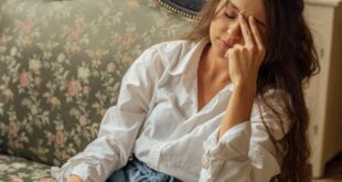 A woman relaxes on a floral vintage sofa in a cozy, light-filled room with plants.