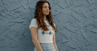 A fashionable woman stands confidently against a blue textured wall, showcasing summer style.