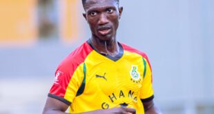 Athlete in Ghana national football jersey holding water bottle outdoors.