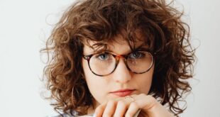 Caucasian woman with curly hair and glasses holding US dollars confidently indoors.