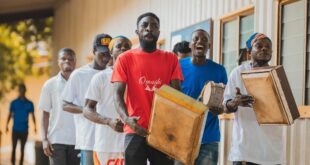 A joyful group of men playing drums and wooden instruments outside in Ghana, showcasing vibrant community spirit.