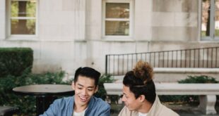 Two young people working together on a laptop outside a building with a classical facade.
