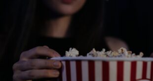 Young woman enjoying movie with 3D glasses and popcorn in a theater setting.