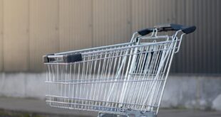 An empty metal shopping cart on a concrete pavement against a grey facade.