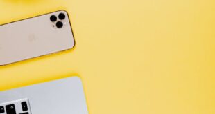 Minimalist workspace featuring a laptop, smartphone, and headphones on a yellow surface.