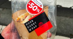 Close-up of a chicken curry wrap with 50% discount packaging held outdoors.