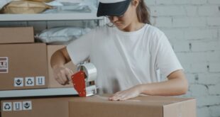 Young female worker sealing cardboard boxes in an indoor warehouse setting.