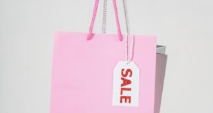 Close-up of a hand holding a pink shopping bag with a sale tag against a white background.