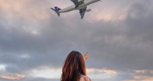 A woman stands in the Dubai countryside pointing at an airplane flying overhead.