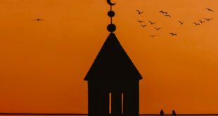 A stunning silhouette of a minaret with birds flying against a warm sunset sky in Accra, Ghana.