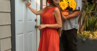 A couple standing at a doorway, holding sunflowers, ready to visit friends.