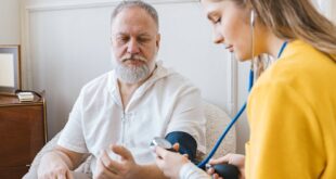 A healthcare professional checks an elderly man's blood pressure in a cozy room.