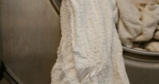 White towels partially hanging from a stainless steel washing machine in a laundromat.