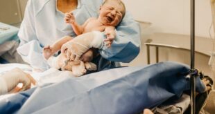 A doctor holds a newborn baby in a hospital setting post-delivery.