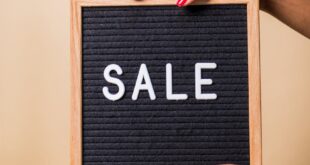 Close-up of hands holding a 'SALE' sign against a beige background, perfect for promotional use.