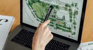 An architect reviews landscape design plans on a laptop, using highlighters and documents at a wooden desk.
