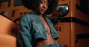 Fashionable woman poses confidently in front of a yellow school bus at dusk.