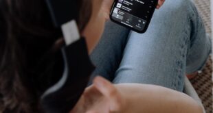 Person wearing headphones, using a smartphone to listen to music in a comfortable setting.