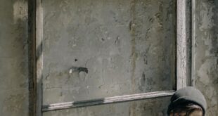 A young man sits eating canned food in an abandoned urban ruin, evoking a post-apocalyptic scene.