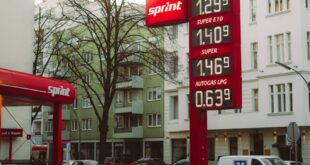 Gas station showing fuel prices in an urban neighborhood with surrounding architecture.