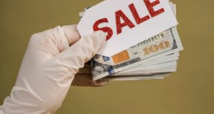 A gloved hand holds a stack of cash and a sale sign, symbolizing discount offers.