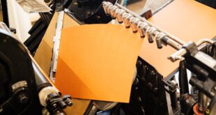 Close-up of a vintage printing press with orange paper, highlighting industrial craftsmanship.