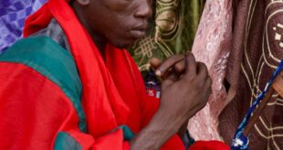 A man from Ghana wearing vibrant traditional clothing, engaged in prayer.