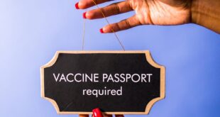 Close-up of hands holding a sign against a blue background reading 'Vaccine Passport Required'.