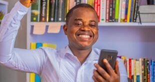 Smiling man in white shirt happily celebrates success with smartphone in hand.
