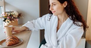 Young woman in a bathrobe enjoys a peaceful morning with coffee and croissant indoors.