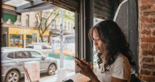 A woman uses her smartphone and laptop in a cozy urban cafe, connected via wireless technology.