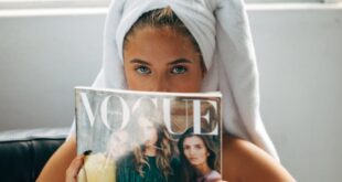Woman wrapped in towel reading Vogue magazine in a relaxed indoor setting.