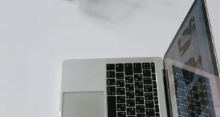 Minimalist scene of a laptop beside a miniature shopping cart symbolizing online shopping.