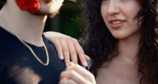 A young couple in a romantic moment outdoors, holding a rose with sunlight casting warm hues.