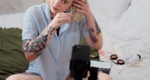 Tattooed woman creating video content at home, using a phone tripod.