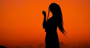 Silhouette of a woman with flowing hair against an orange sunset in Ghana. Perfect golden hour capture.